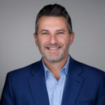 Professional headshot of CFAC Board Member Rob Cowgur wearing a blue blazer and light blue collared shirt, smiling against a light gray background.