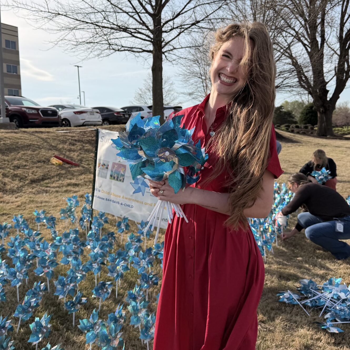 Person in a red dress holds blue pinwheels while standing in a pinwheel garden during a Child Abuse Prevention Month awareness campaign.