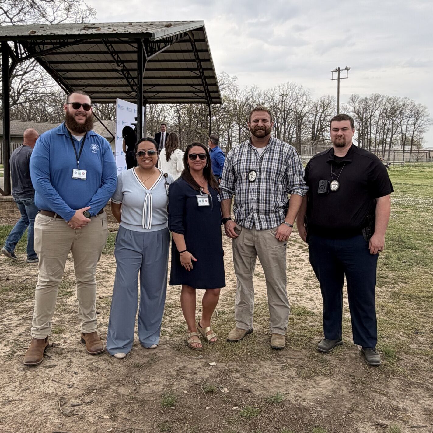 Group photo of community partners and public safety professionals gathered outdoors near a pavilion during a child abuse prevention awareness event.