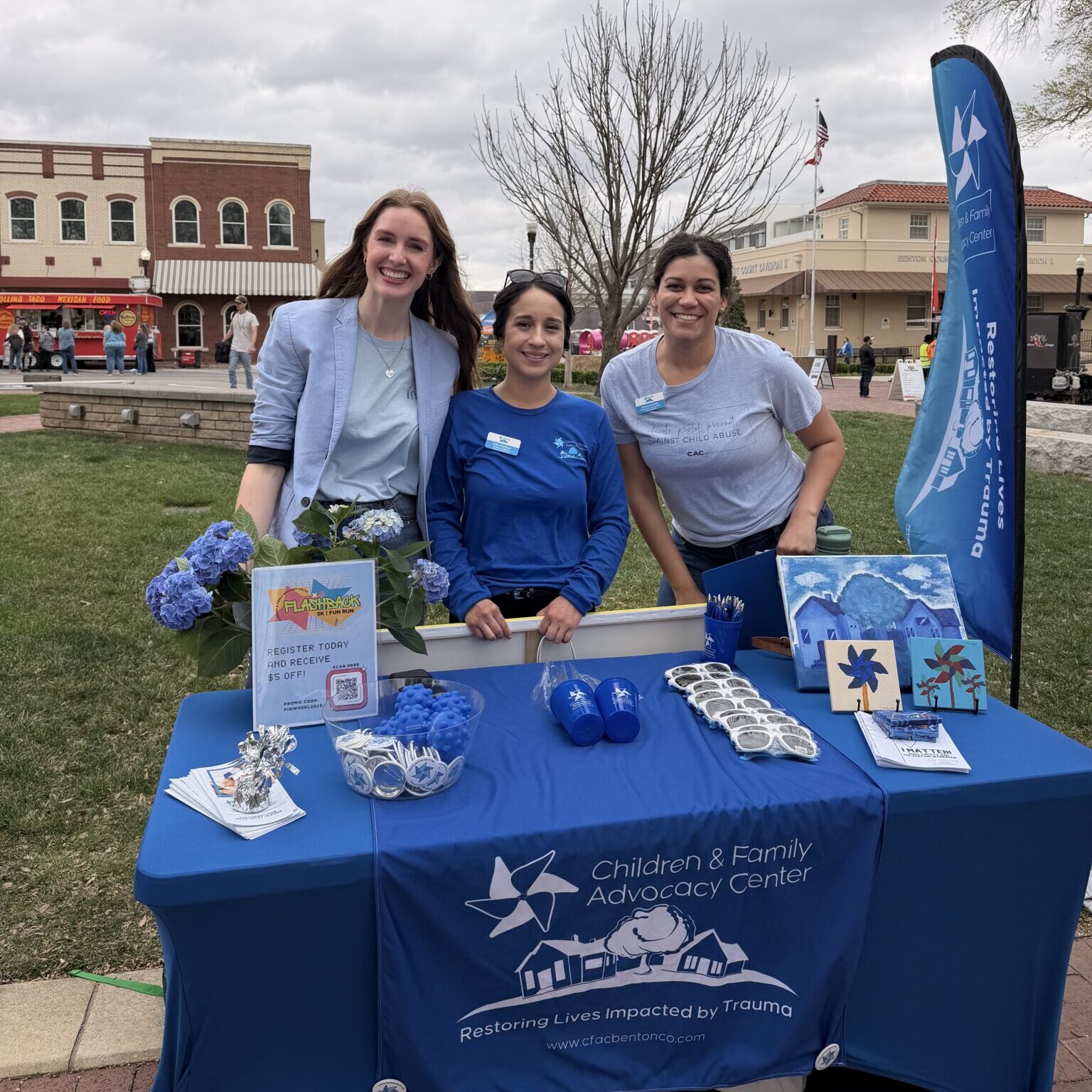 Three Children & Family Advocacy Center team members stand behind an information table with educational materials and giveaways at a community awareness event.